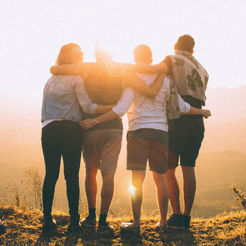 Thousandfold Brand Positioning — Four people stand with their arms around each other looking towards the light as a community of calling-driven individuals determined to support, lift up, and amplify the unique callings of each of its members. 