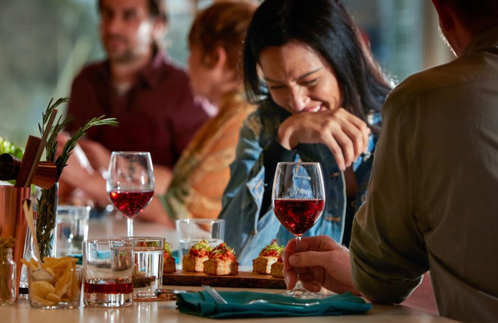 Woman laughing with wine and appetizer at table in Everyday Kitchen.