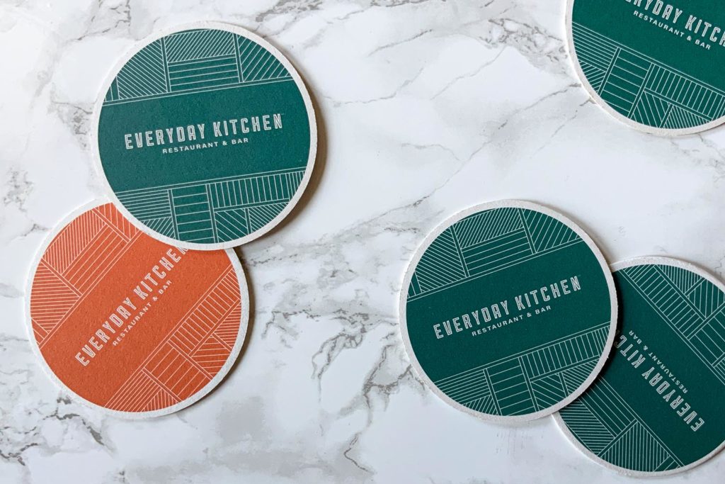 Everyday Kitchen coasters in teal and orange on marble table.