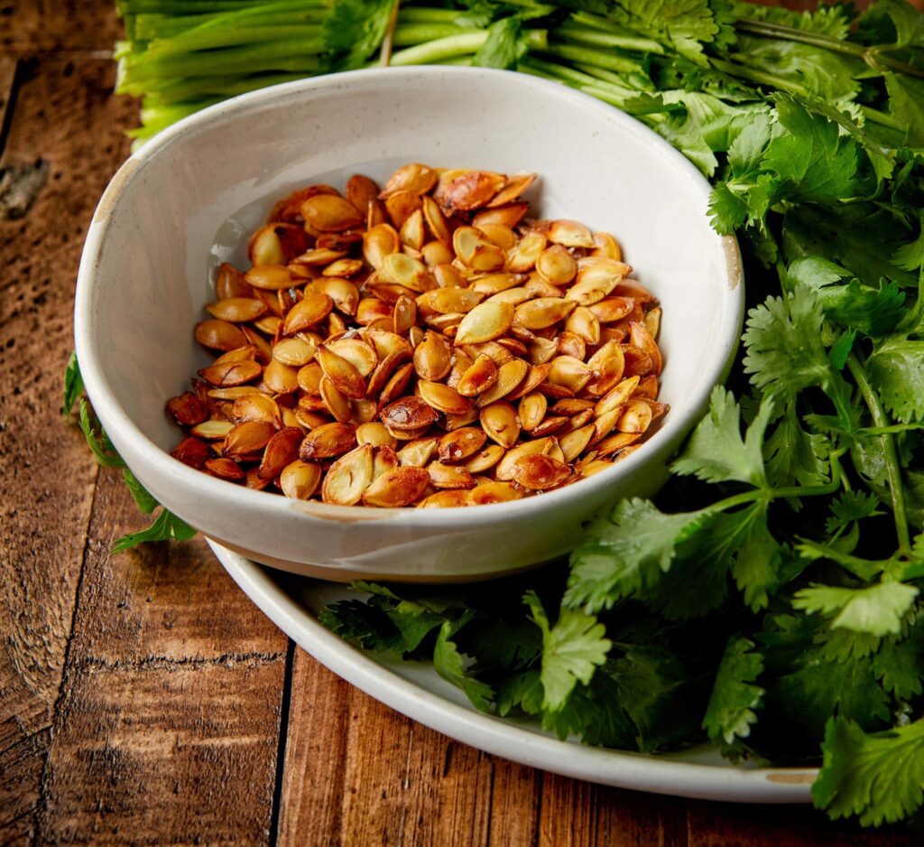 Toasted pumpkin seeds in bowls with herbs on wooden table.