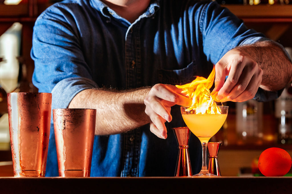 Everyday Kitchen's brand identity shown over signature branded photography of a bartender making a cocktail on fire. 