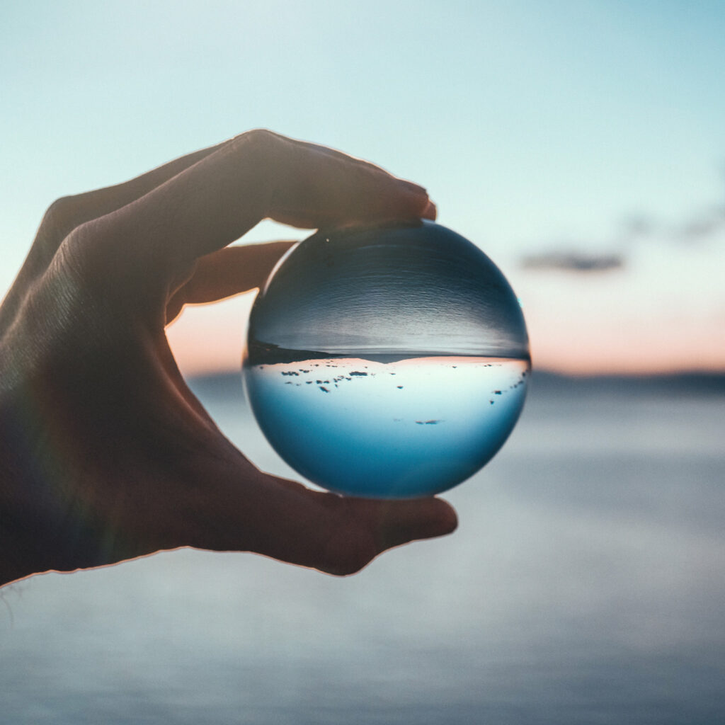 On Purpose Now Brand Positioning — hand holding glass sphere in front of the ocean and sunset to show clarity and focus.