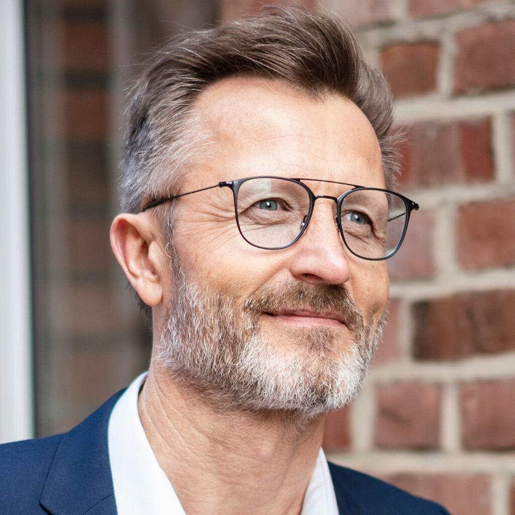 Beyond the Crucible Brand Positioning — Middle-aged man with glasses and a short grey beard smiling genuinely while looking to the right. 